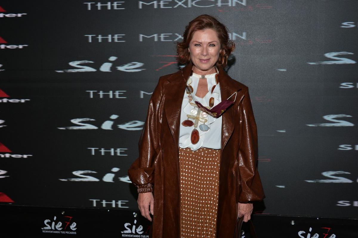 Leticia Calderon poartă o fustă maro, o bluză albă și un palton de aceeași culoare cu cea a fustei