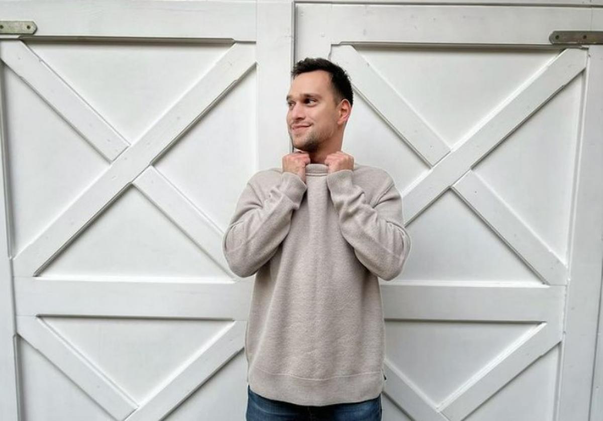 Vlad Gherman poartă blugi și o bluză maro deschis