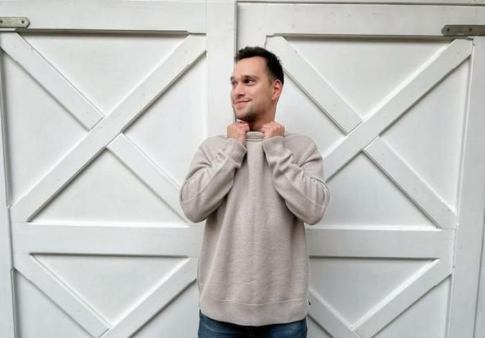 Vlad Gherman poartă blugi și o bluză maro deschis