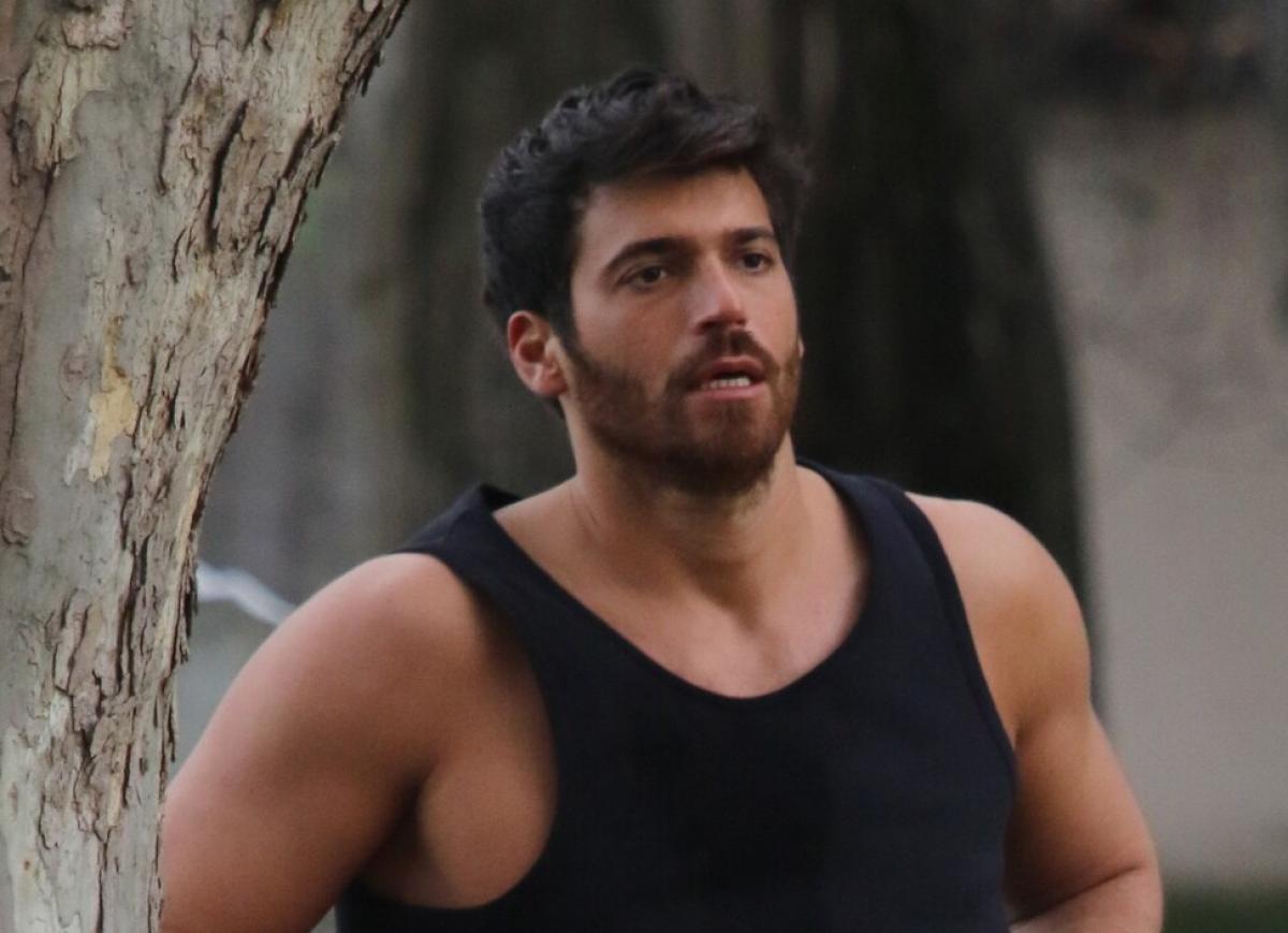 Actorul turc Can Yaman, îmbrăcat într-un maiou negru, sprijinit de un copac