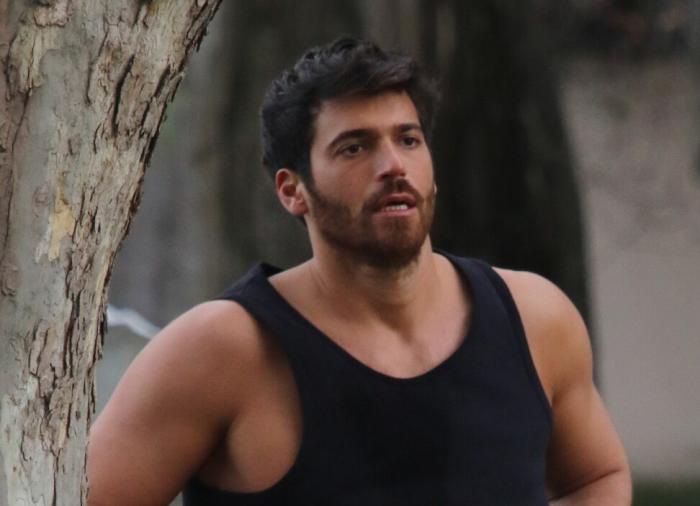 Actorul turc Can Yaman, îmbrăcat într-un maiou negru, sprijinit de un copac