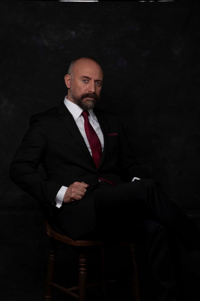 Halit Ergenç fotografie de studio pe fundal negru, în timp ce stă jos, fotografiat pe fundal negru