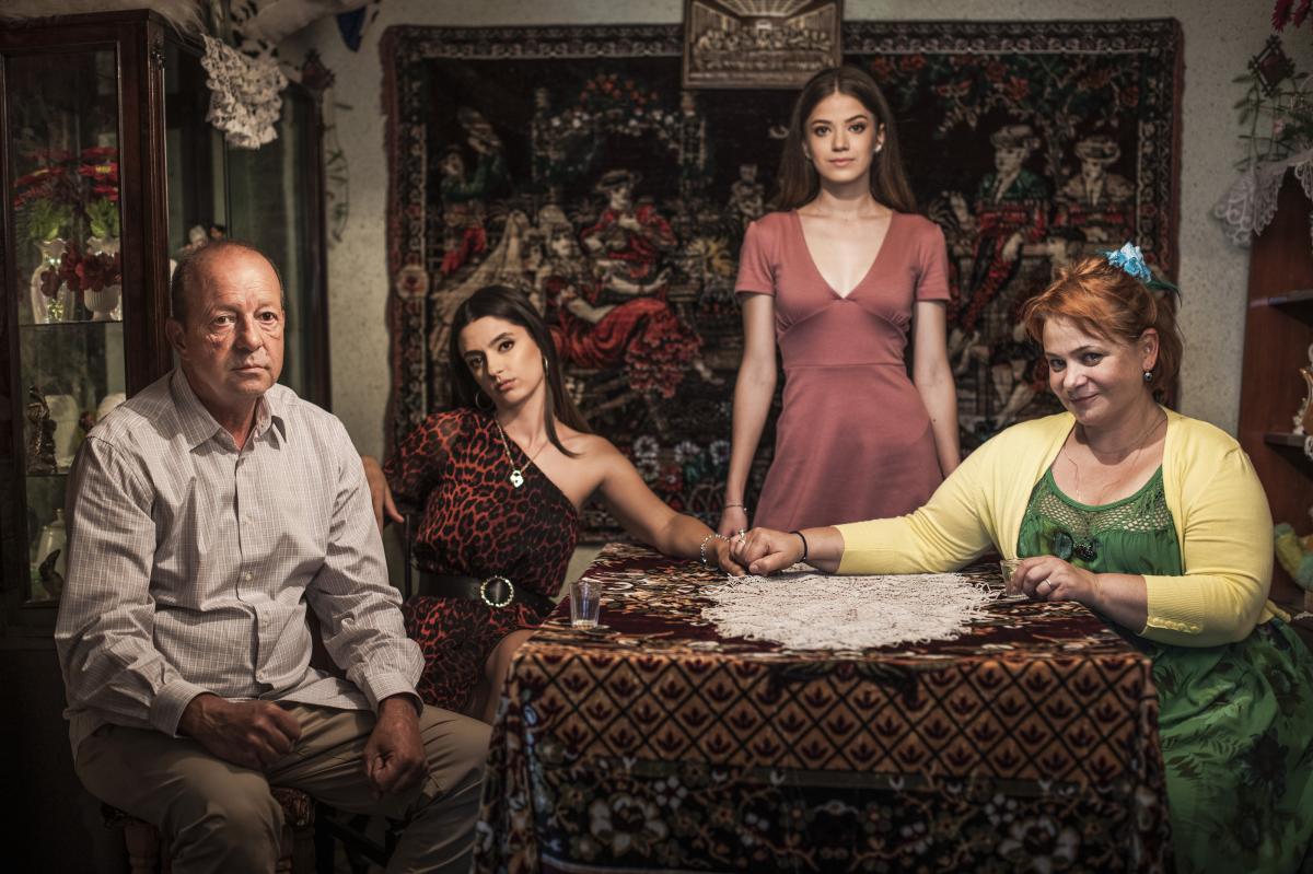 Actorii din Adela: personajele Nuți, Mitu, Adela și Andreea Achim stau la masă, în casa lor de la țară, cu un covor pe perete, în fundal