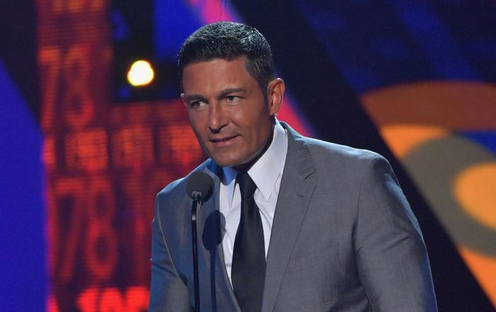 Actorul Fernando Colunga vorbind pe scenă, la microfon, îmbrăcat cu un costum gri