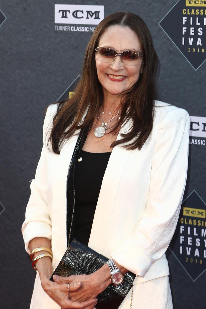 Olivia Hussey la 67 de ani pe covorul roșu, îmbrăcată într-un costum alb