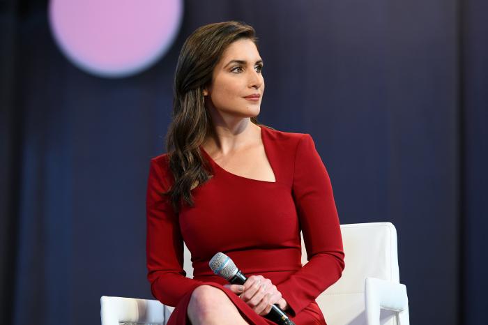 Katiria Soto la o emisiune, cu microfonul în mână, îmbrăcată într-o rochie roșie