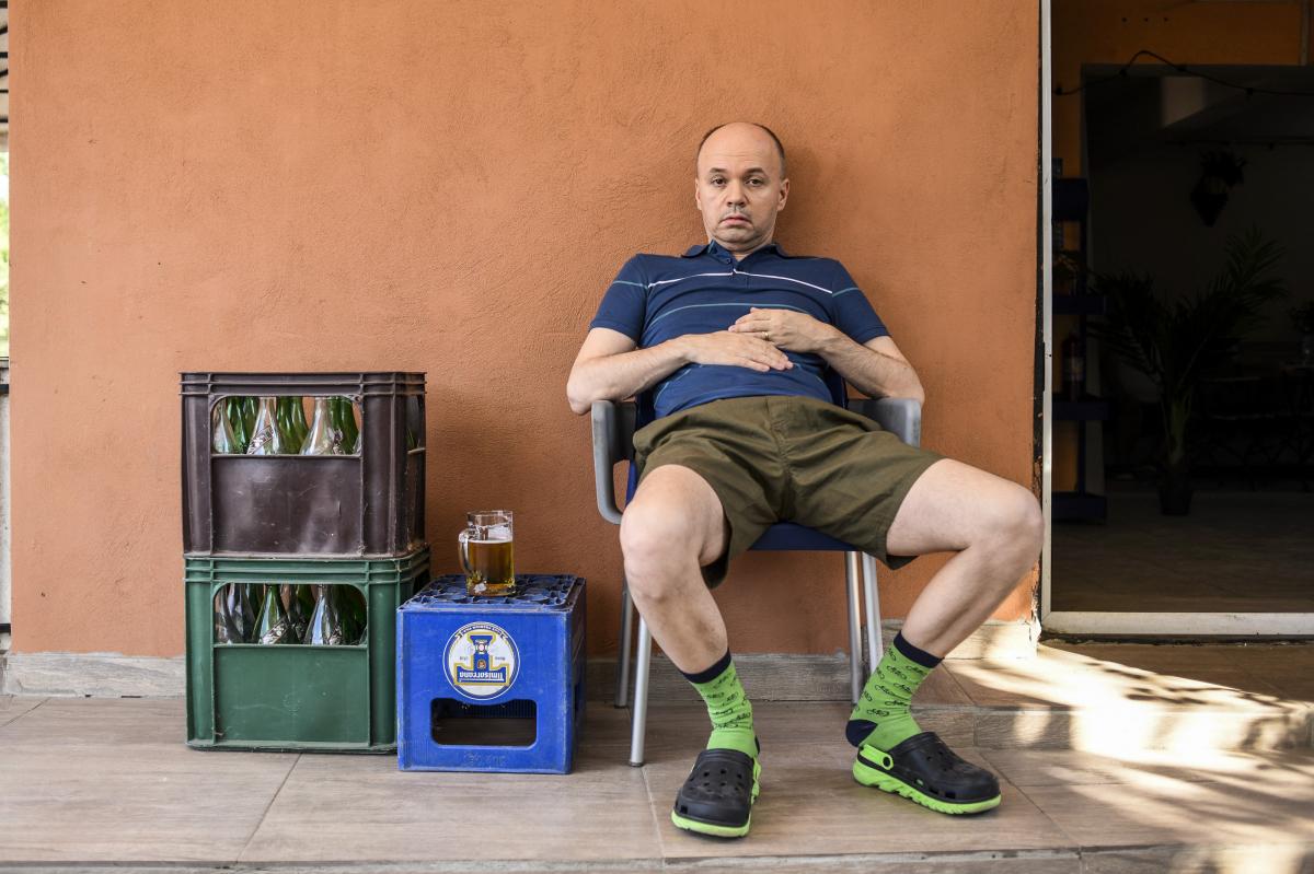 Mircea Gheorghiu pe platoul de filmare al serialului Adela, stă pe un scaun de plastic alături de câteva baxuri de bere