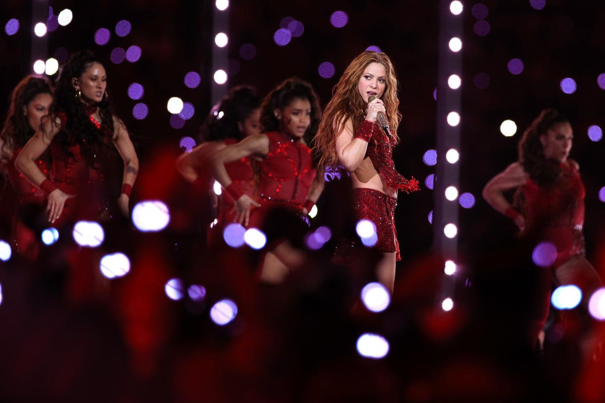 Shakira în timpul unei prestații live pe scenă, îmbrăcată în roșu, alături de dansatoare