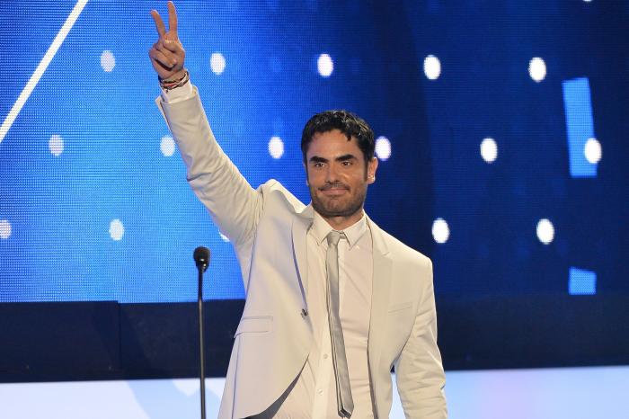 Actorul Lincoln Palomeque, pe scenă, îmbrăcat în costum alb, fundal albastru