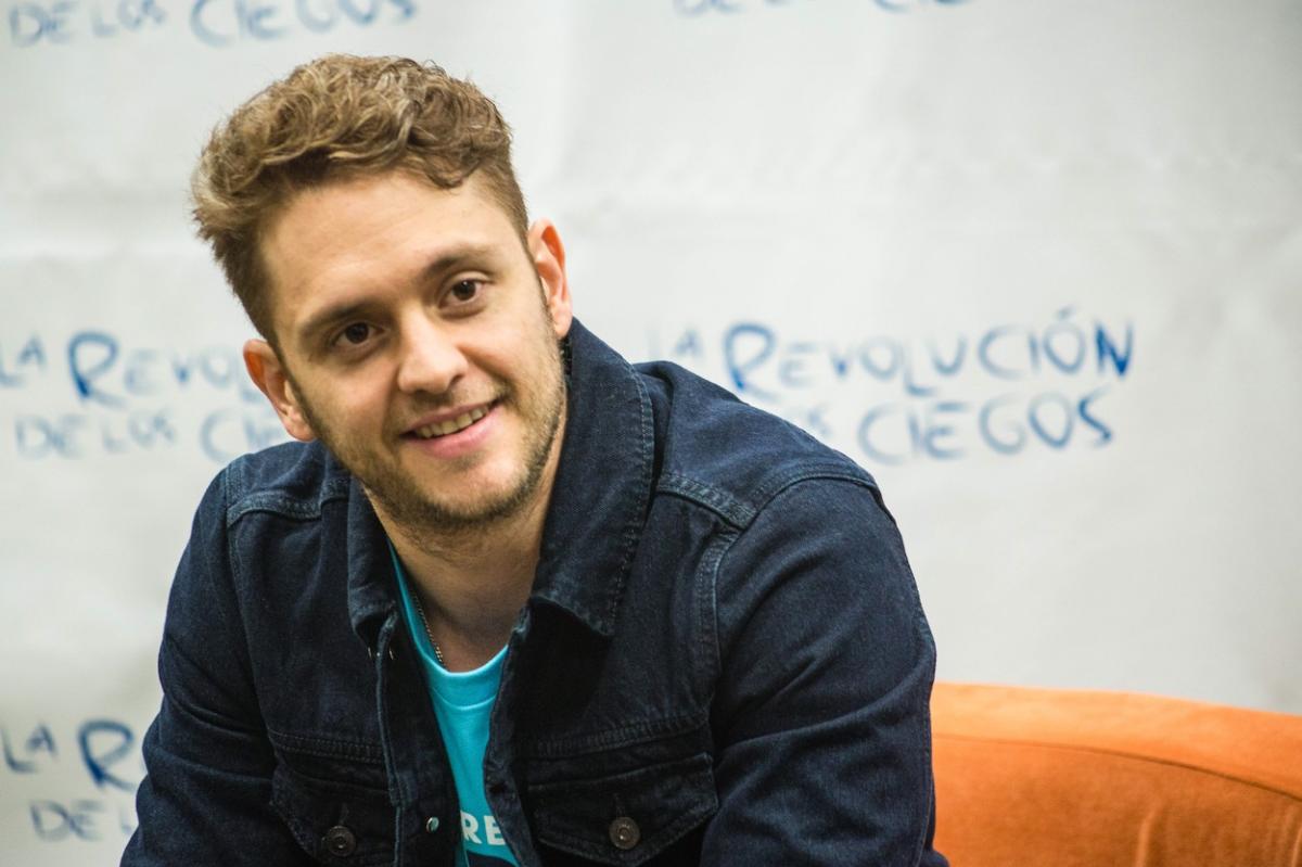 Christopher Uckermann poartă un tricou albastru și o geacă de blugi