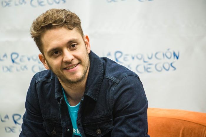 Christopher Uckermann poartă un tricou albastru și o geacă de blugi