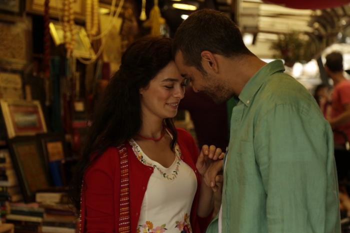 Özge Özpirinççi poartă o bluză albă și un pulover roșu