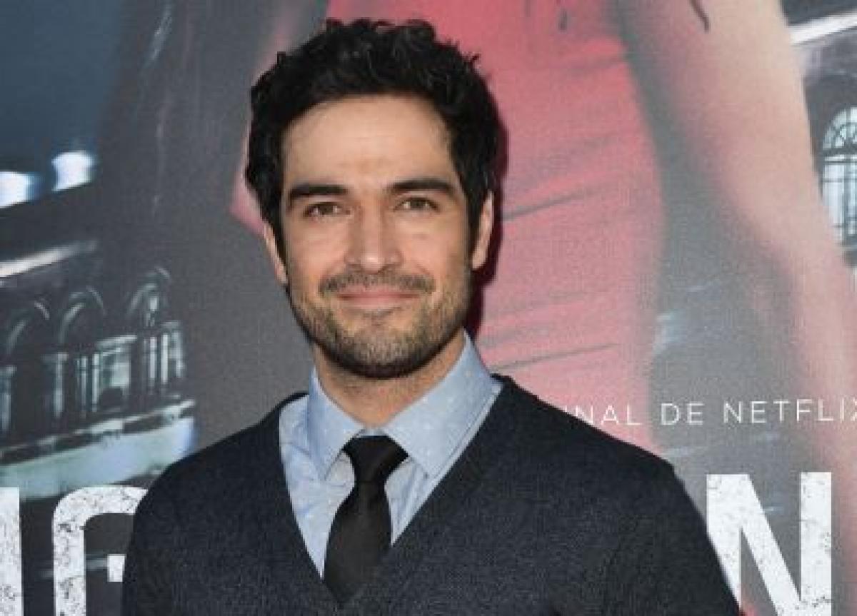 Alfonso Herrera poartă o cămașă albastră și un pulover de culoare închisă
