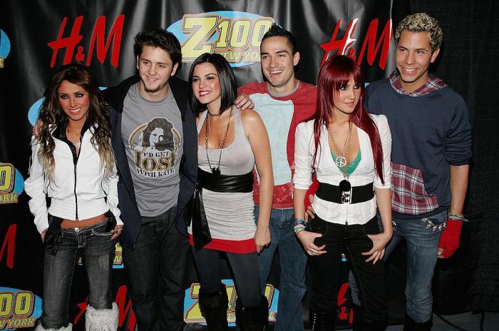 Alfonso Herrera poartă blugi și o bluză roșie cu gri