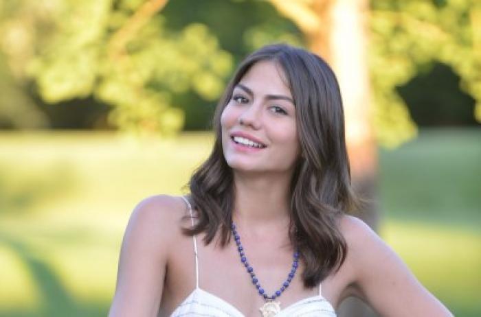 Demet Özdemir poartă un top alb cu bretele foarte subțiri și are părul desprins