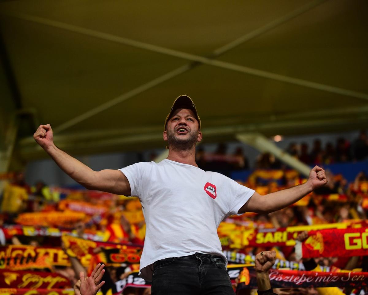 Rıza Kocaoğlu poartă un tricou alb și o șapcă