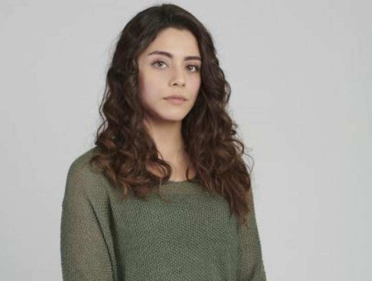 Sıla Türkoğlu poartă un pulover verde și are părul desprins și ondulat