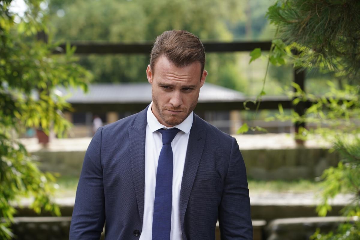 Kerem Bürsin poartă o cămașă albă și un costum închis la culoare