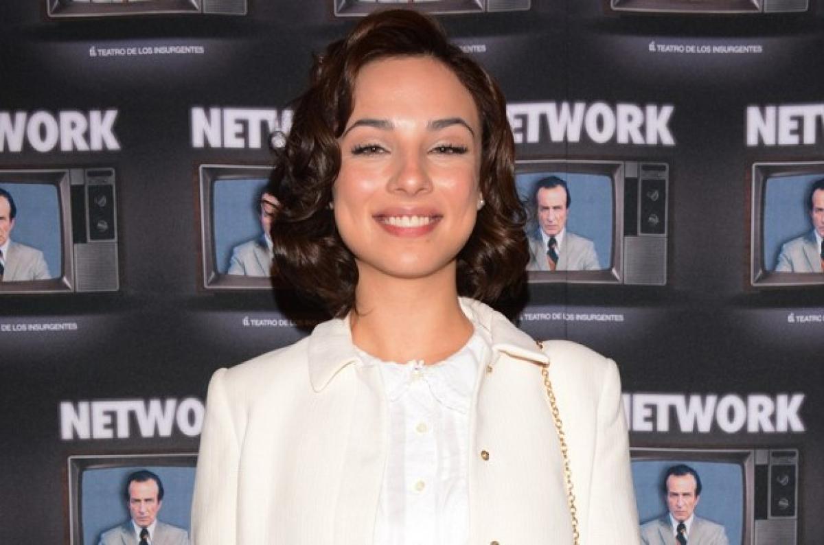 Fiona Palomo poartă o bluză albă și un sacou de aceeași culoare și zâmbește