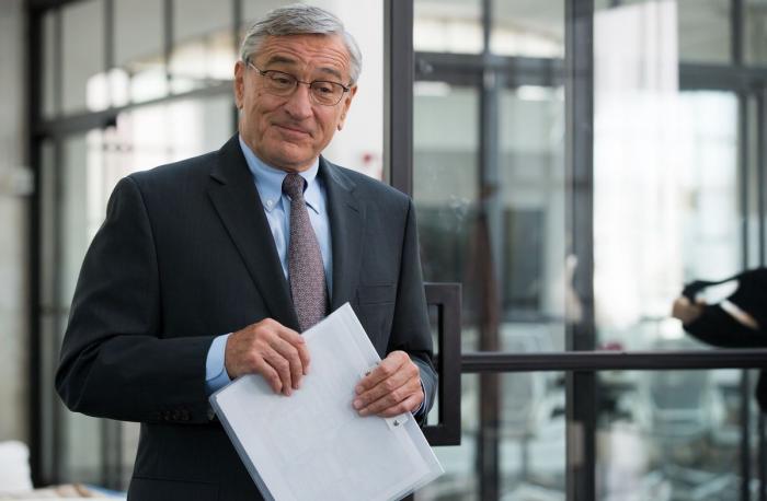 robert de niro poartă un costum și ține în mână un dosar