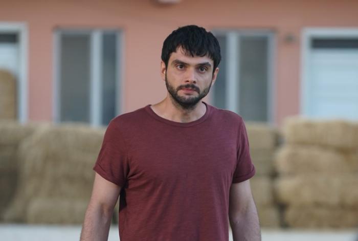 Toprak Can Adıgüzel poartă un tricou vișiniu și are barbă și părul negru