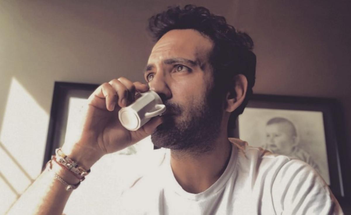 Buğra Gülsoy poartă un tricou alb și bea o ceașcă de cafea