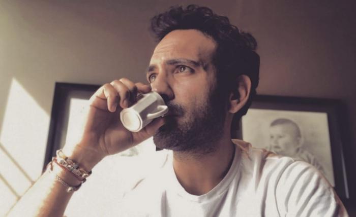 Buğra Gülsoy poartă un tricou alb și bea o ceașcă de cafea