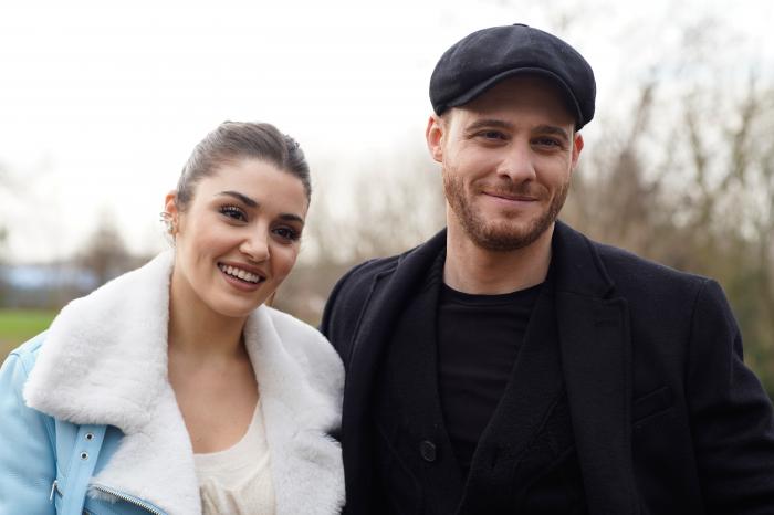 Hande Ercel zâmbește și stă lângă Kerem Bursin care poartă o pălărie închisă la culoare