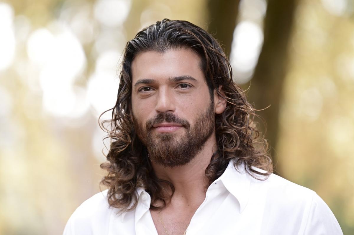 Can Yaman poartă o cămașă albă cu mâneci lungi și are părul desprins, ondulat