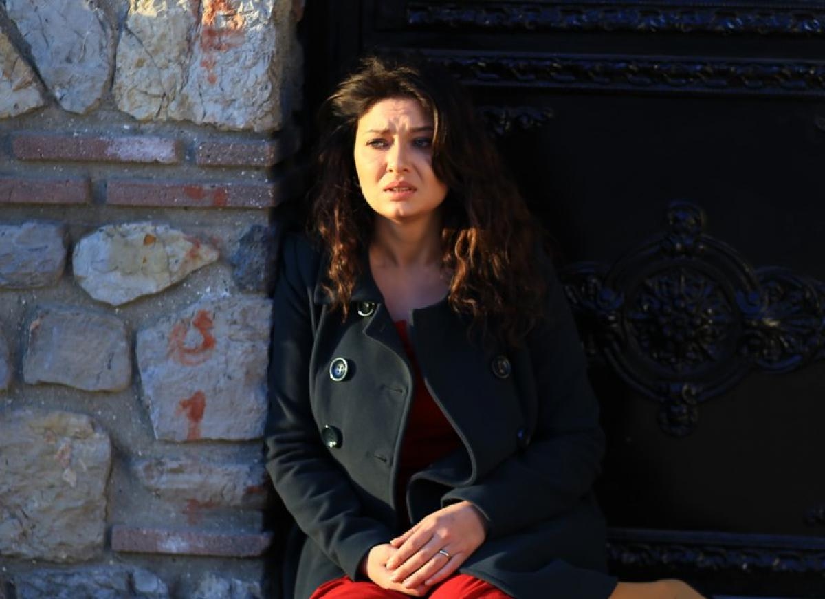 Nurgül Yeşilçay poartă o rochie roșie și un palton negru și are părul desprins