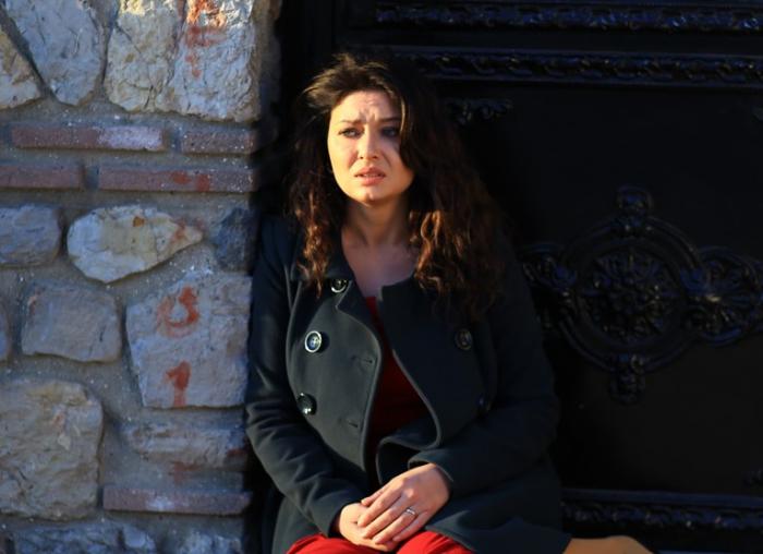 Nurgül Yeşilçay poartă o rochie roșie și un palton negru și are părul desprins