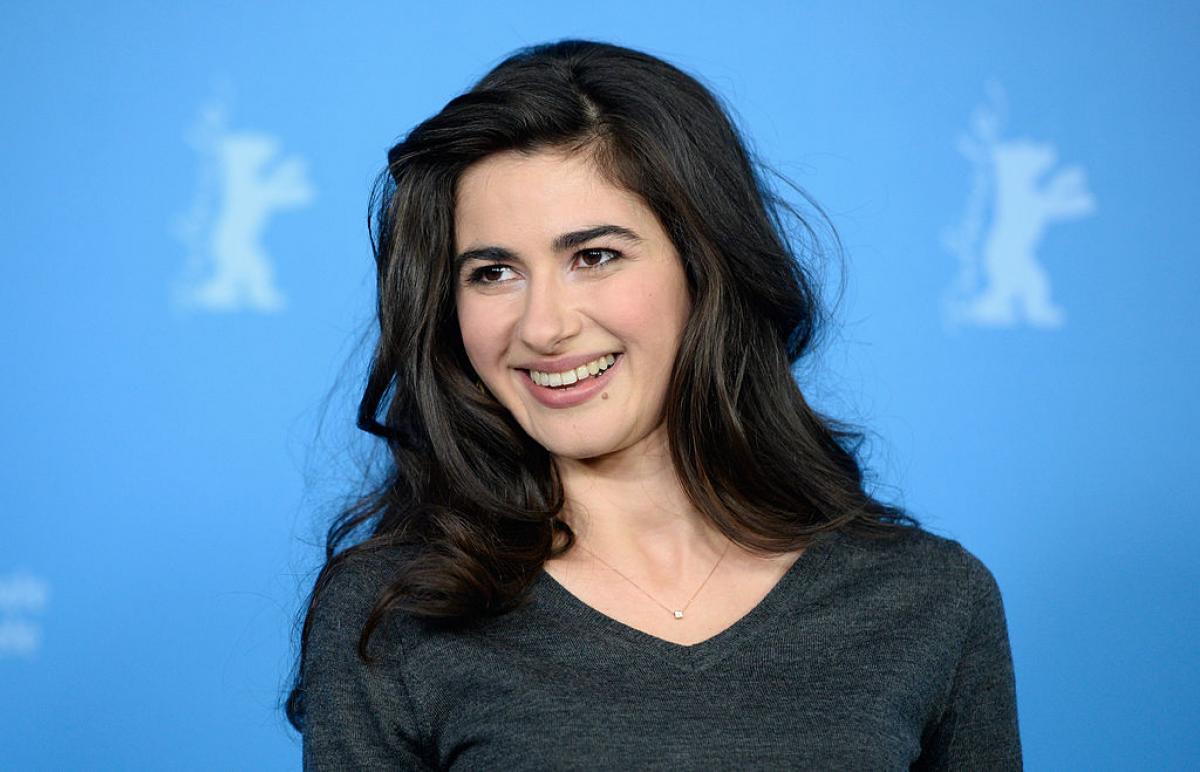 Nesrin Cavadzade poartă o bluză cu mânecă lungă, părul desprins și ondulat și zâmbește