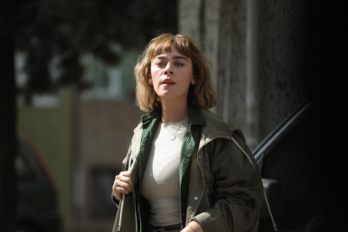 Demet Evgar poartă o bluză albă și o geacă verde închis