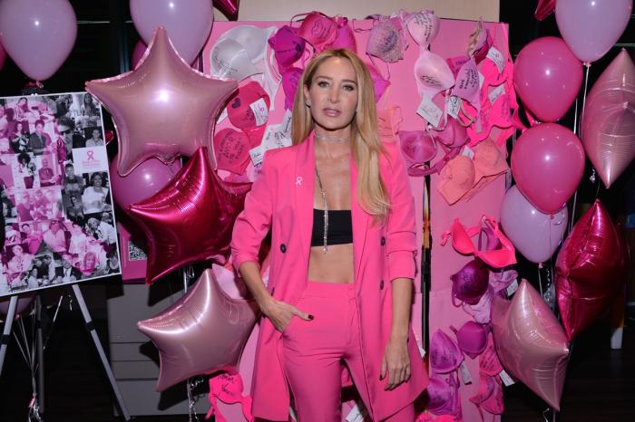 Geraldine Bazán poartă un costum roz, top negru și își ține mâna dreaptă în buzunar. Are părul lung și îl poartă desprins