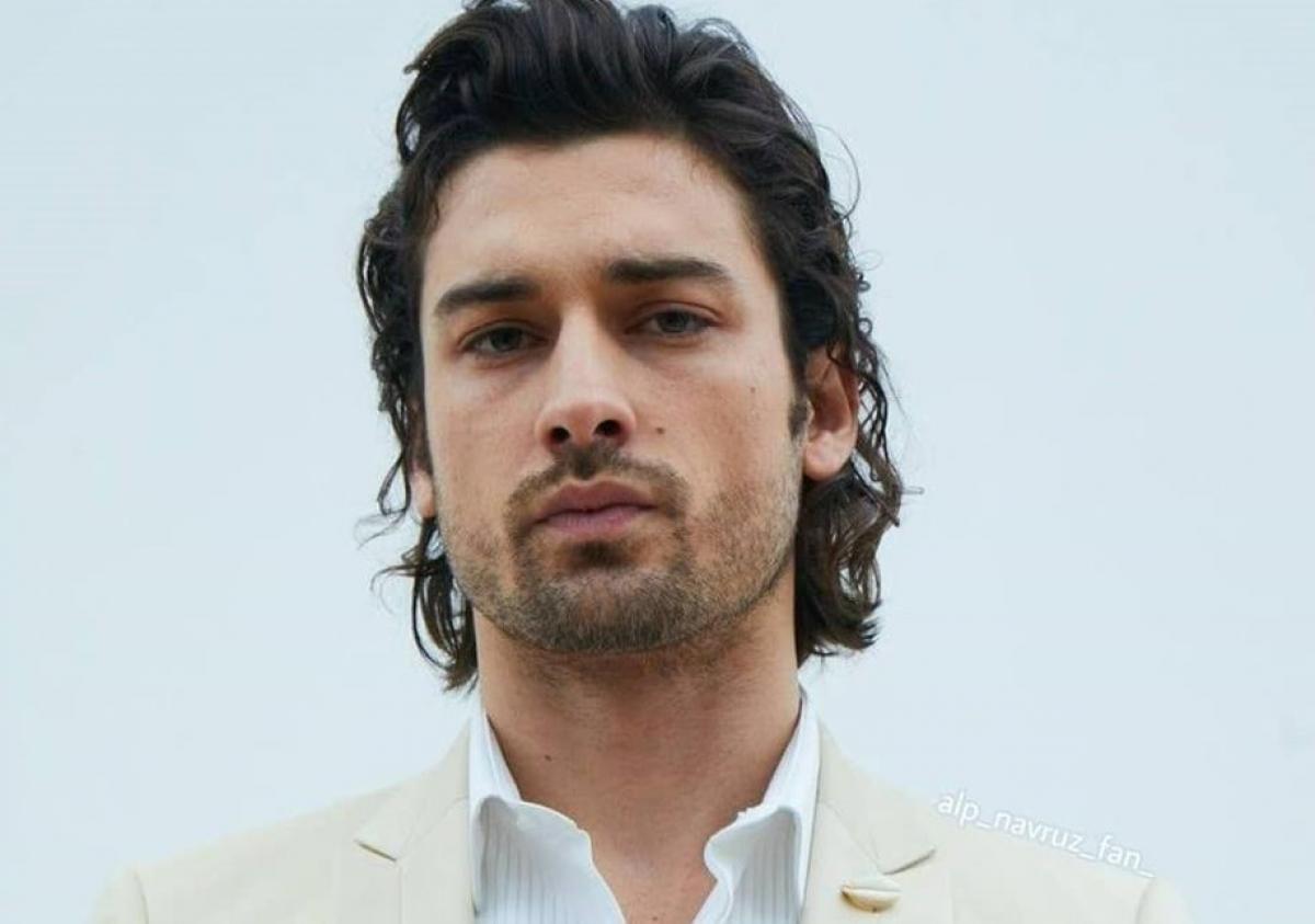 Alp Navruz poartă o cămașă deschisă la culoare și un costum alb