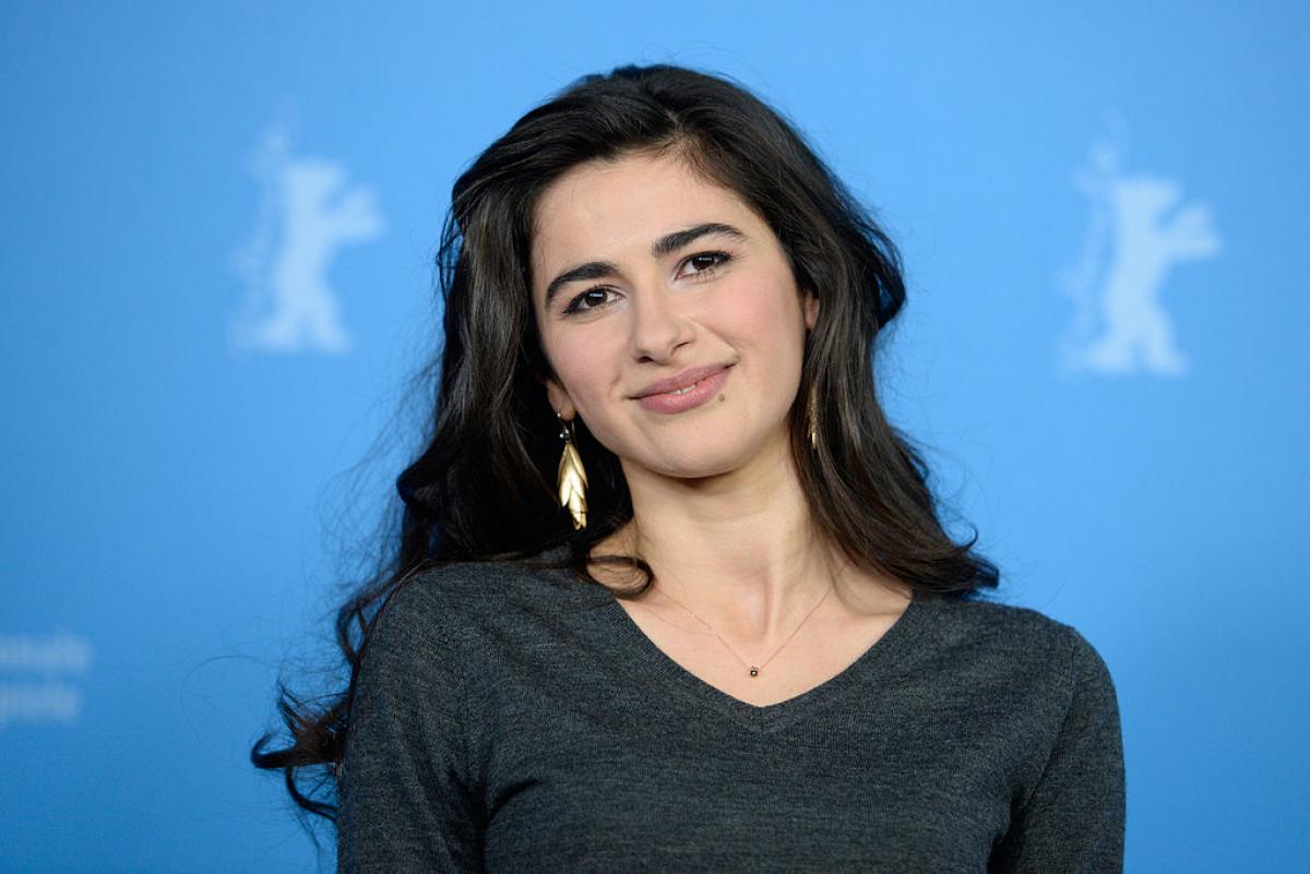 Nesrin Cavadzade poartă o bluză cu mânecă lungă, părul desprins și ondulat și zâmbește