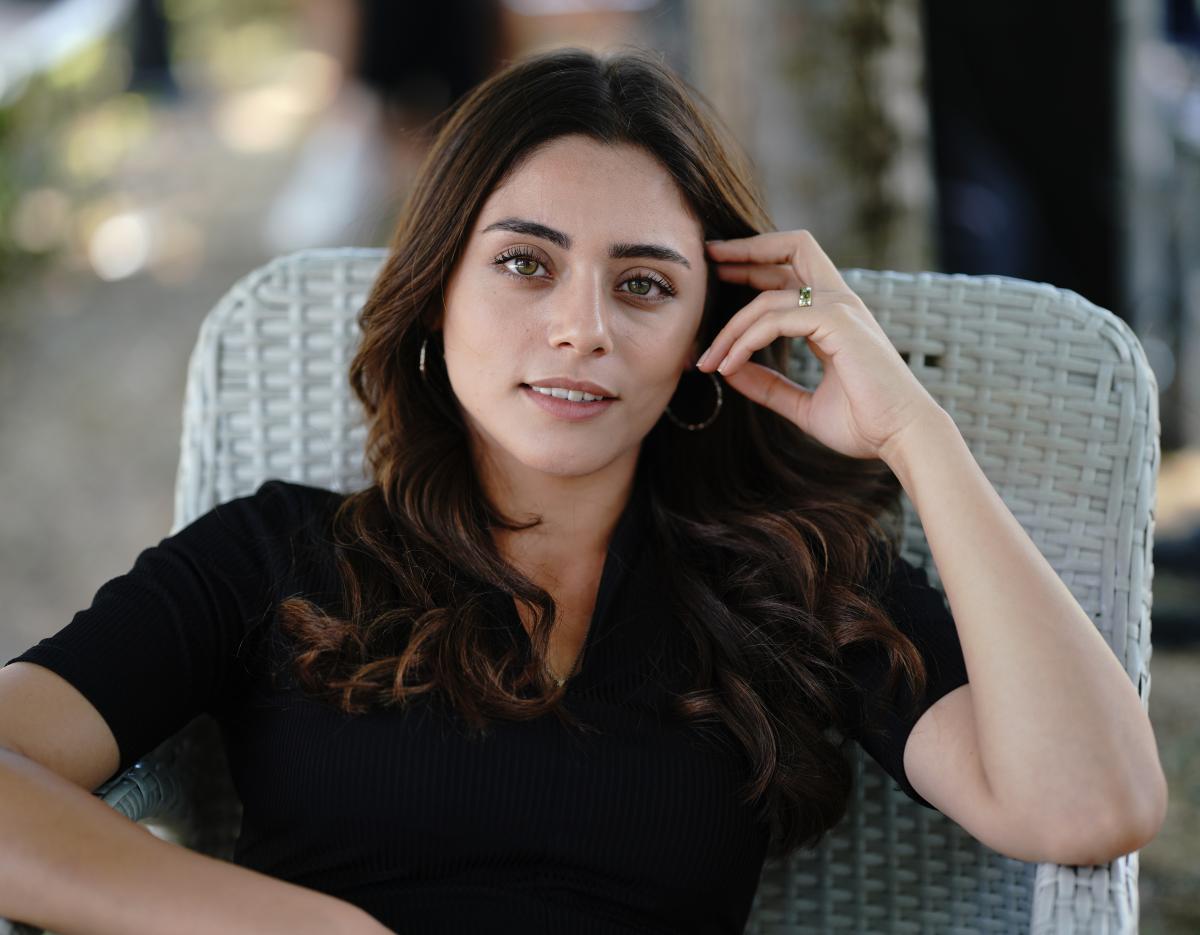 Sila Turkoglu poartă o rochie neagră cu mâneci scurte și își ține mâna stângă în dreptul urechii