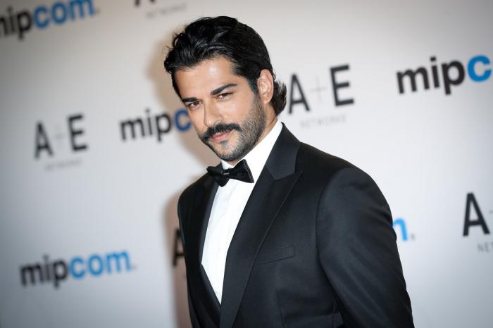 Burak Özçivit poartă o cămașă albă și sacou negru și are mustață
