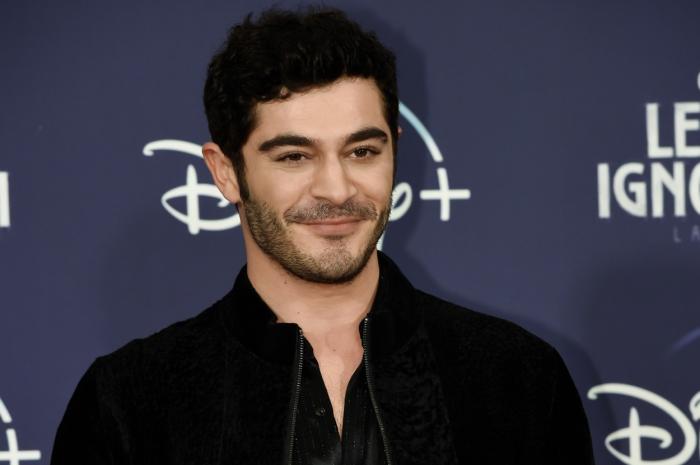 Burak Deniz poartă o cămașă neagră deschisă la gât