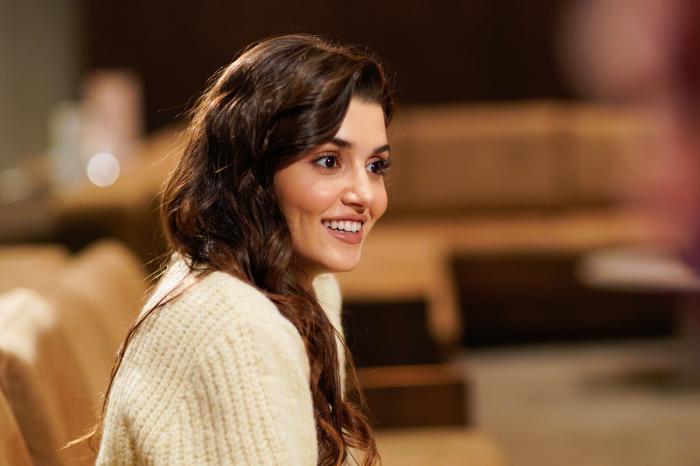 Hande Erçel poartă o bluză albă și zâmbește