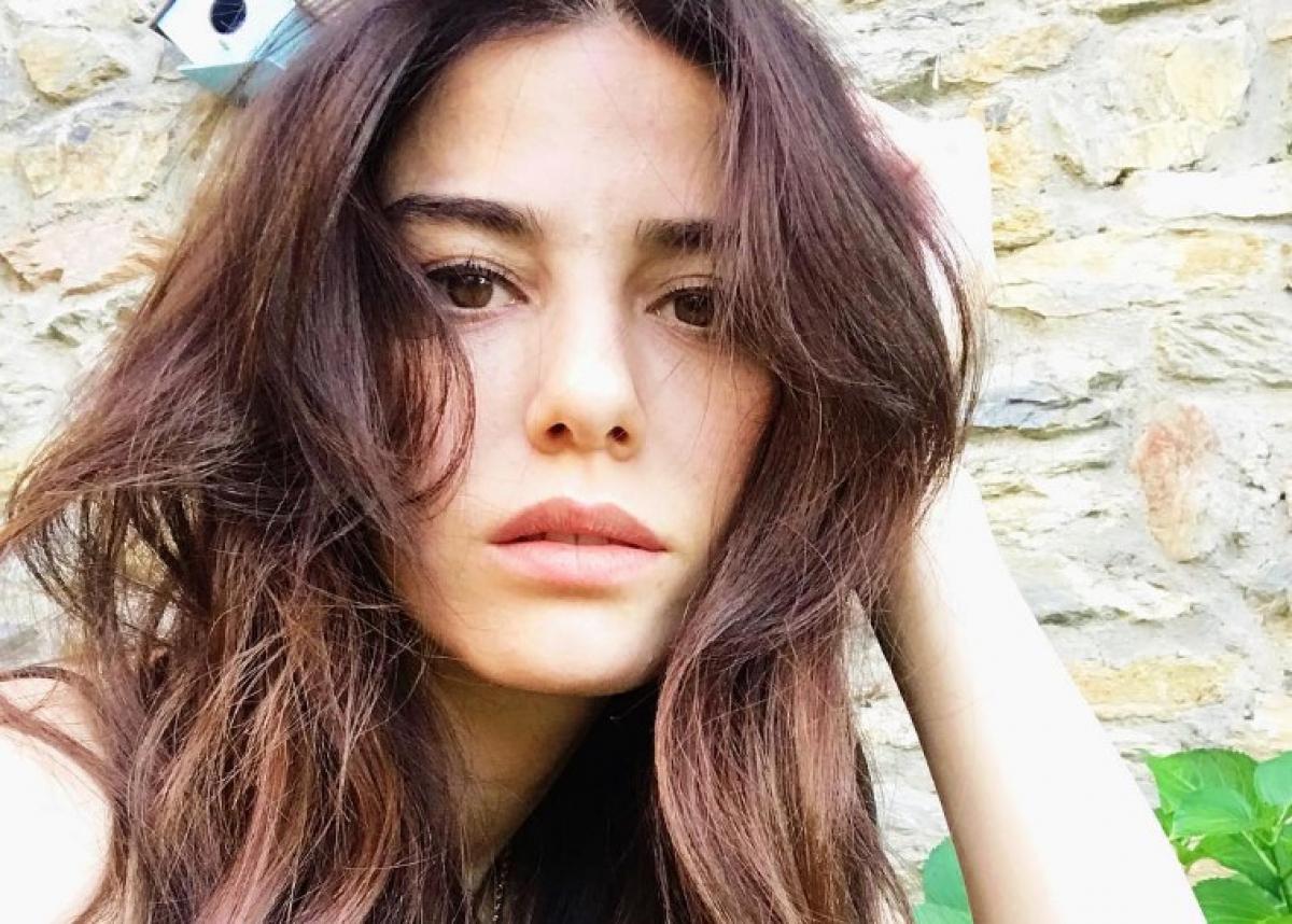 Ozge Gurel poartă părul desprins și își ține mâna stângă la tâmplă