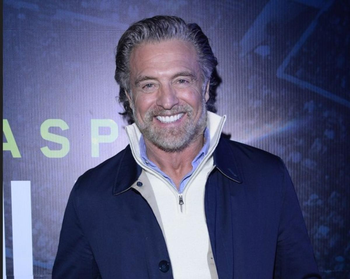 Juan Soler poartă o geacă albastră, un pulover alb și zâmbește