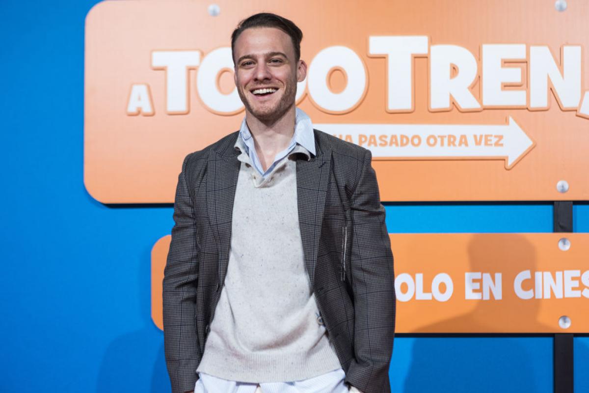 Kerem Bursin poartă o pereche de pantaloni deschiși la culoare și stă cu mâinile în buzunare