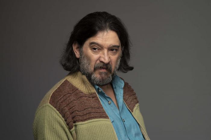 Hasan Ballıktaş poartă o cămașă albastră și un pulover maro