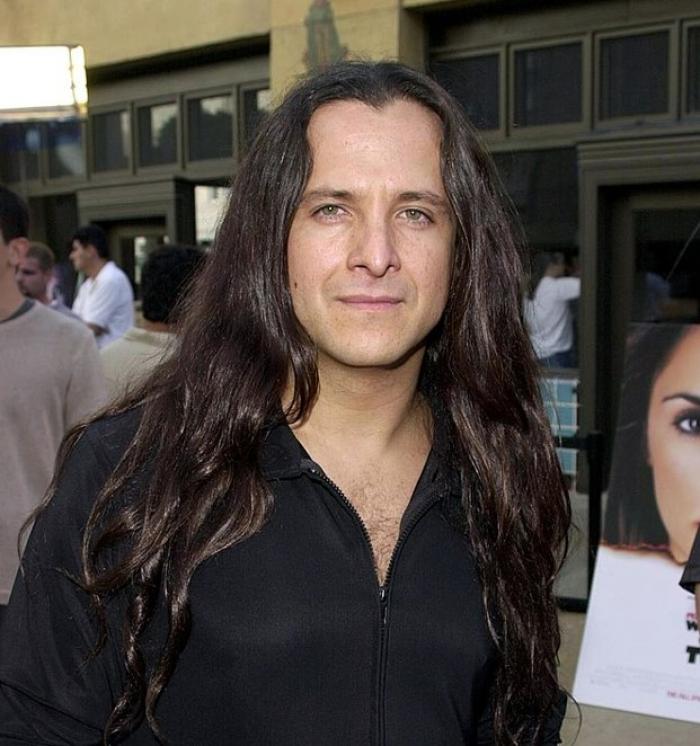 Eduardo Palomo are părul lung și poartă o bluză neagră cu mâneci lungi