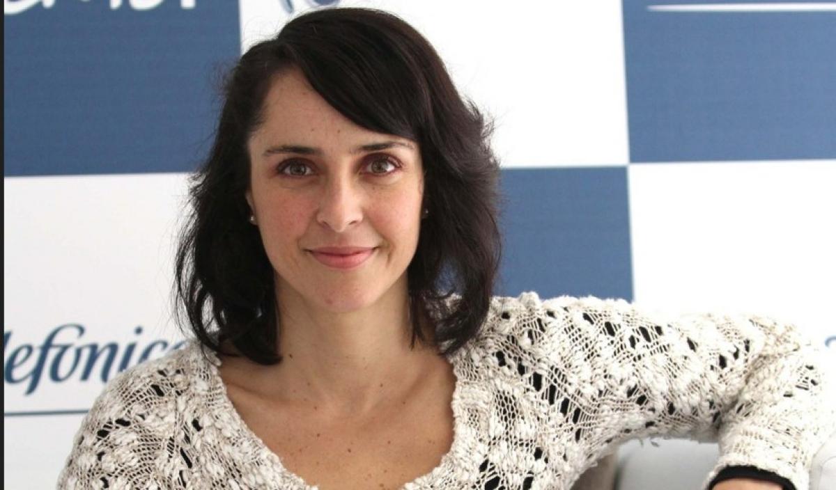 Irán Castillo poartă o bluză albă, zâmbește și are părul despins