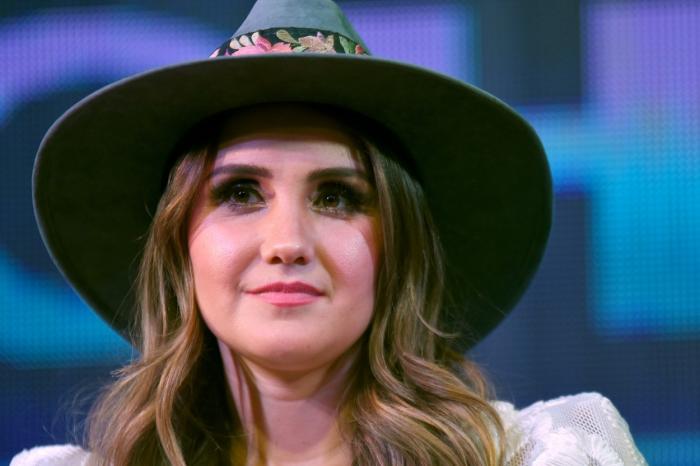 Dulce María se află în cadrul unei conferințe de presă și poartă o pălărie cu boruri largi. Vedeta are părul desprins și un machiaj simplu