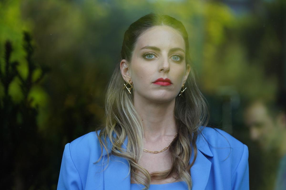 Bige Önal poartă un costum albastru, are părul desprins și ruj roșu