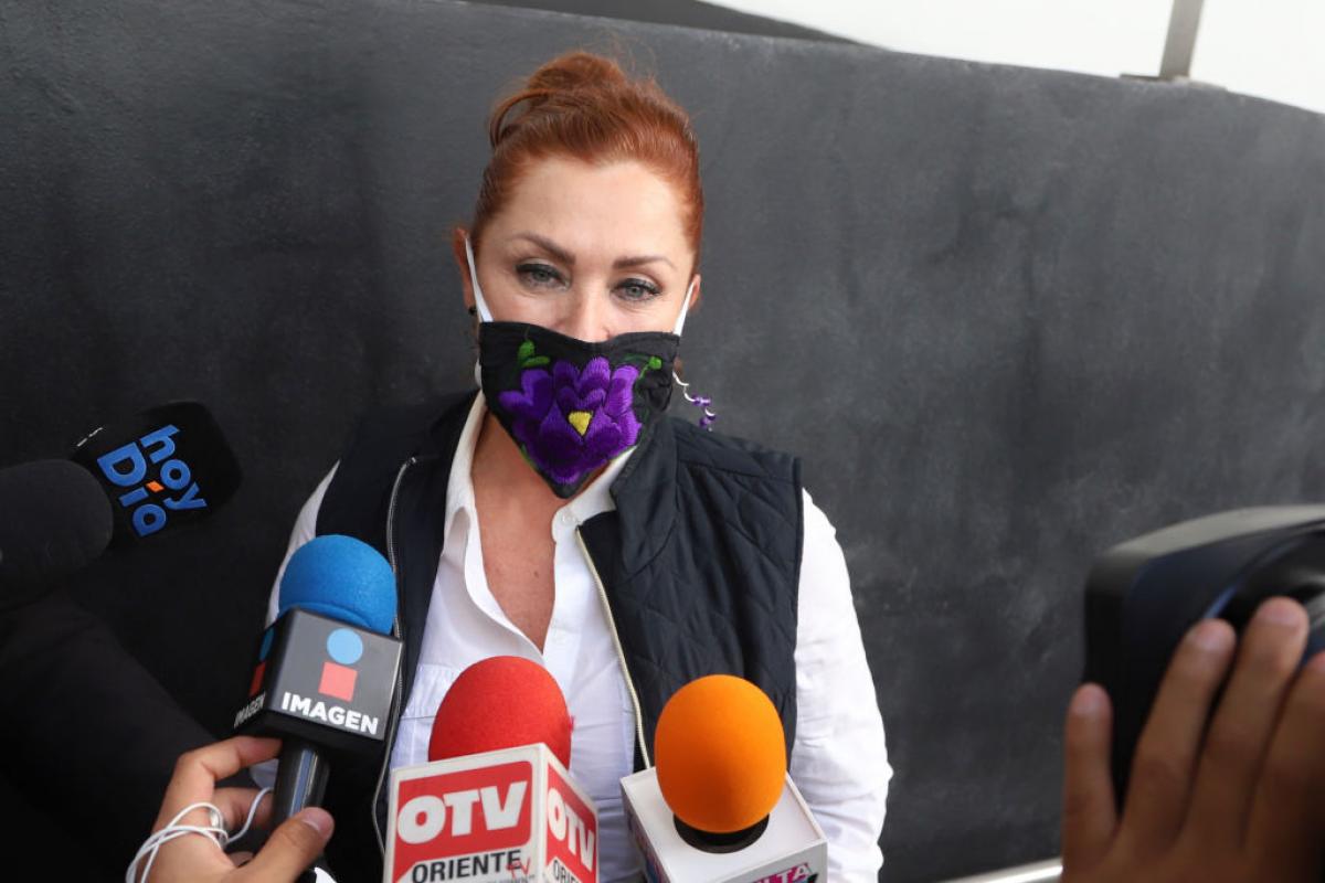 Lety Calderón poartă o cămașă albă și o vestă neagră. Are părul prins