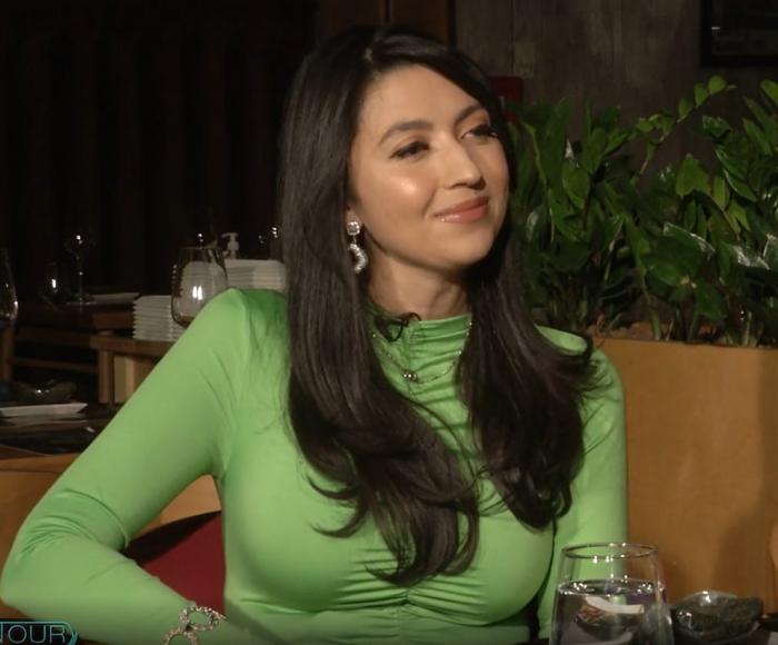 Maria Andreea poartă un pulover verde cu mâneci lungi și are părul negru. Artista latino îl poartă desprins și are un machiaj de seară